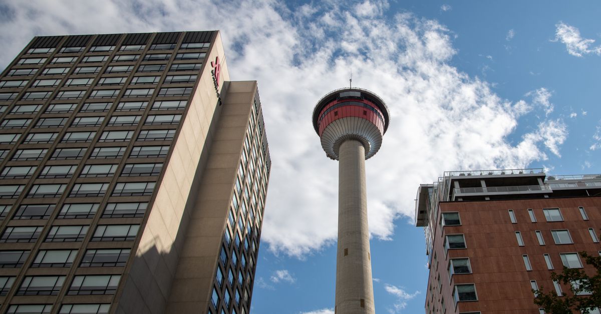 View of Calgary Tower surrounded by modern urban buildings against a blue, cloudy sky.